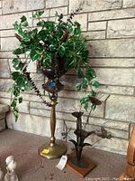Tall metal pedestal with urn planter holding artificial variegated leaves green foliage placed against stone wall