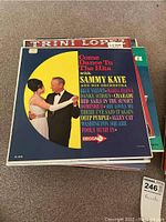 Top vinyl record album titled 'Come Dance To The Hits with Sammy Kaye and His Orchestra'. Colorful cover with dancing couple.