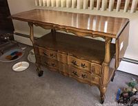 Wood serving cart front view showing two drawers with metal pulls, open bottom shelf, scalloped edges on top, and rounded legs on casters.