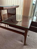 Side view of 2-tier wooden side table showing glass top, cane side panel, and brass leg tips