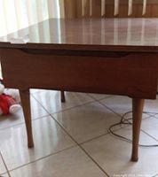 Front angle view of the wooden side table showing color, drawer front, and tapered legs.