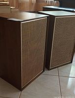 Two rectangular Sears Silvertone speakers with wood veneer cabinets and fabric front grilles, placed side by side on tiled floor.