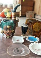 Photo shows ceramic pipe, several ashtrays, coasters in a caddy, lighter and brandy bottle holder on table.