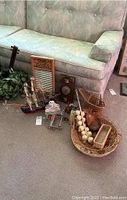 Photo of vintage kitchenware and decorative items arranged on carpet next to sofa, includes baskets, Columbus washboard, vintage scale, string of garlic, apple corer, and barometer.
