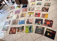 Overview photo showing 36 vintage vinyl records laid out on a tiled floor, displaying cover art from a range of artists and genres including Hawaiian music and dance compilations.