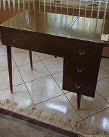 Wooden sewing cabinet with three drawers featuring brass pulls, showing wood grain and scratches on the top surface.