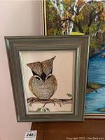 Framed stylized owl painting in a gray wood frame, showing detailed feather design, sitting on a branch with a muted white background.