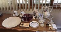 Overview of all items on table including plates, figurines, glasses, teacups, red glass bowls, and plaques.