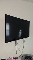 Front view of black Samsung flat screen TV mounted to wall with cables hanging below
