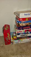 Stack of various board games including Uno Attack, Heads Up, Taboo, Guess Who, Twister, Clue, Sorry, Family Feud, Life, and Monopoly showing box condition and titles.