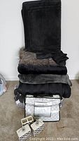 Stacked bedding including comforter, multiple blankets, and new king sheet set in package with black and white bathroom dispensers and toothbrush holder in front
