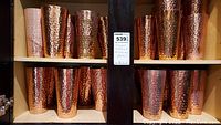 Shelf with over 25 copper colored hammered metal drinking glasses, arranged in rows.