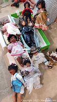 Overhead view of eight dolls, some lying on floor and some in green box with bubble wrap
