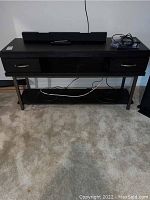 Front view of the black entertainment console with two drawers and a sound bar on top.