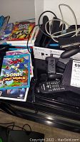 Stack of Wii/Wii U game cases (Sonic Lost World, Guitar Hero Live, Just Dance) alongside assorted remotes and cables