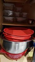 Stacked glass Pyrex food storage containers with clear lids, with metal mixing bowls and red plastic colander partially visible