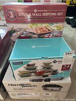 Boxes of Member's Mark double wall serving set, 24-piece glass food storage set, and Hamilton Beach roaster oven stacked together