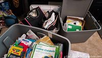 Three large plastic bins filled with various school supplies including notebooks, totes, and writing tools