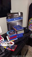 PS4 slim console top with stack of game cases and original box behind