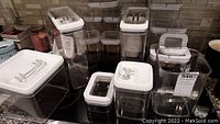 Clear plastic rectangular and square food storage containers with white lids, some with clear inset window covers, arranged on dark countertop.