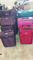 Multiple suitcases grouped including purple, pink, red and blue colors showing front and top views.