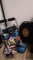 Photo showing AB Firm Pro abdominal exercise machine on top of the Compact Strider box, Gold's Gym mini trampoline, 10 lb medicine ball, and assorted workout videos stacked on floor.