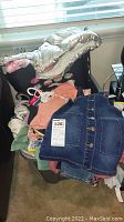 Large tote filled with children's clothing including jackets, tops, denim dresses, and sock bundles.