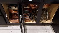 Photo showing multiple copper-colored Tramontina pots, skillets, and glass lids stored in a cabinet.
