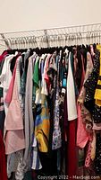 Photo of various women's tops hanging on rack, assorted colors and styles.