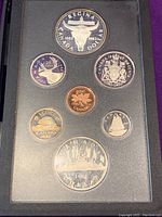 Reverse sides of 1882 and 1982 Canadian proof coins showing various designs including cow skull, Toronto skyline, caribou, beaver, and coat of arms in display case.