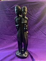 Front side view of the ebony wood carving showing two of the figures, one holding a water vessel and another holding a child.