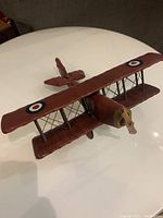 Angled view of dark red canvas-covered WW1 biplane model showing wooden propeller and rigging between wings.