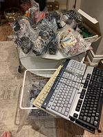Photo showing a plastic basket and table covered with clear plastic bags containing numerous wired computer mice, cables, and assorted computer parts.