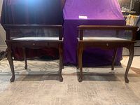 Pair of wooden Bombay Co. end tables with glass tops and Queen Anne style legs shown side by side.