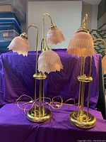 Pair of brass Victorian style table lamps with pink frosted glass shades on purple cloth background.