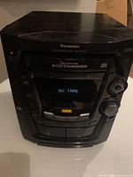 Front view of the Panasonic stereo system showing control panel, cassette deck with 'NO TAPE' displayed, and 5 CD changer branding