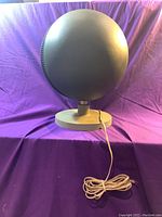 Front view of large black spherical speaker mounted on circular base, with white cable coiled on the surface below.