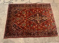 Full view of small Persian area rug showing red background with floral and geometric motifs.