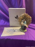 Full view of the figurine, original box, book and gift tag on purple background