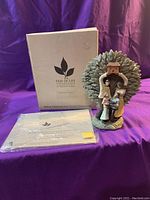 Full view of the Tree of Life Collection figurine with its box and sealed book/gift tag in front, displayed on a purple fabric.