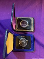 Two silver dollars in black velvet-lined cases, one dated 1972 and the other 1976, showing front face with detailed designs.