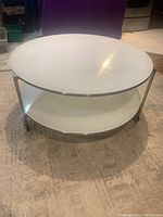 Front view showing both white glass tiers, metal frame, and caster wheels.