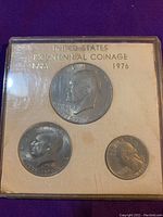 Obverse side of bicentennial coins showing profiles of Eisenhower, Kennedy, and Washington in a protective display with title card.
