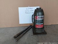 Front view of the 12 ton black NAPA hydraulic bottle jack with two metal handle sections beside it. Jack has carrying handle attached and visible labels.