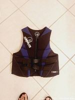 Single blue and black Hyperlite INDY neoprene life jacket laid flat on tiled floor showing front zipper and adjustable straps.