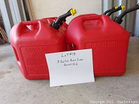 Six red plastic 5 gallon gas cans with yellow cap and black flexible spouts, displayed on a concrete floor.