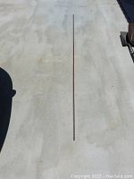 Full length view of the 8-foot copper grounding rod laid out on a concrete floor, showing its length and surface staining.