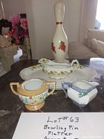 Photo of bowling pin door stop, platter, gravy boat, sugar bowl and milk pitcher with handwritten lot number sign