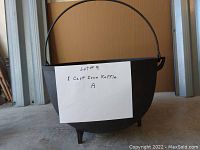 Front view of cast iron kettle showing the front, legs, and handle with a label identifying it as Lot #9