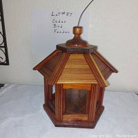 Photo of a hexagonal cedar wood bird feeder with six glass panels and a pointed roof, showing new condition and a metal hanging wire.